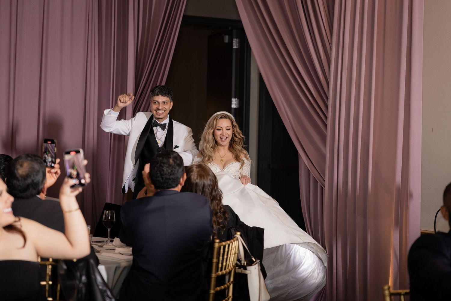 A couple makes their grand entrance into their wedding reception through pink curtains.