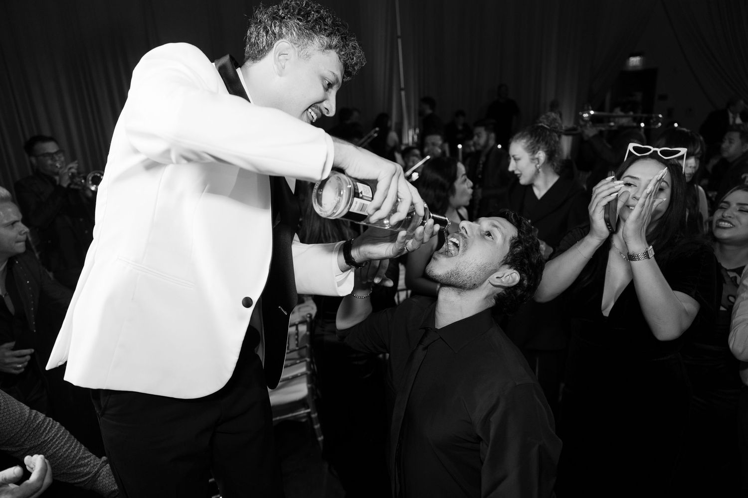 Black and white photo of guests sharing drinks at an energetic wedding reception.