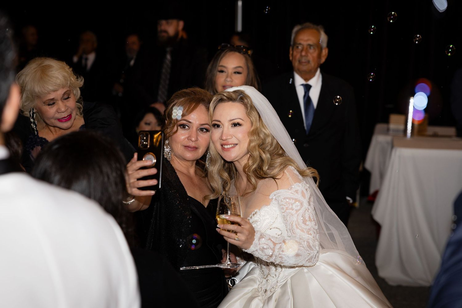 Wedding reception guests mingle and celebrate in an elegantly lit ballroom setting.