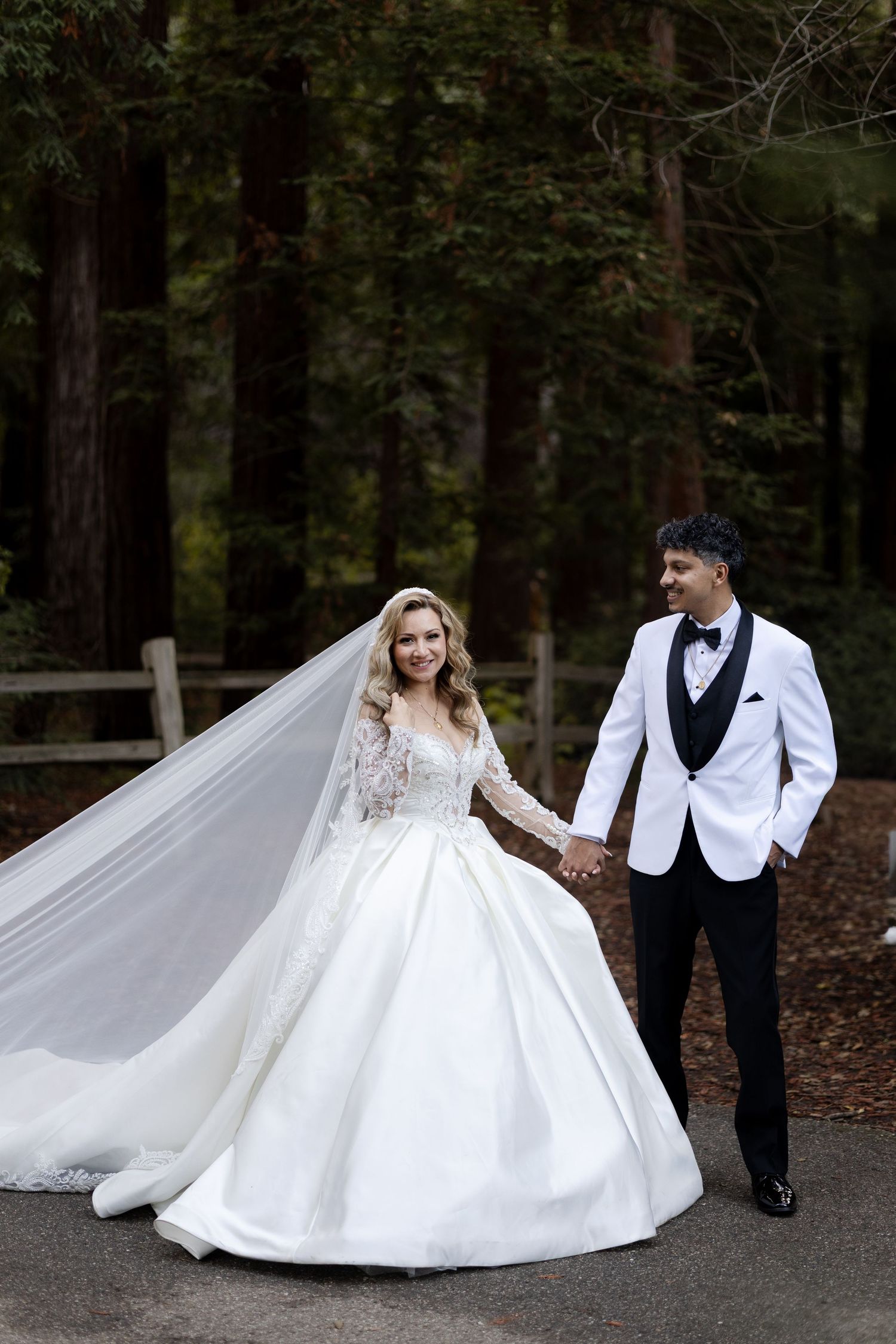 A romantic wedding photo of a couple in a forest setting, with the bride wearing a flowing white gown and long veil.
