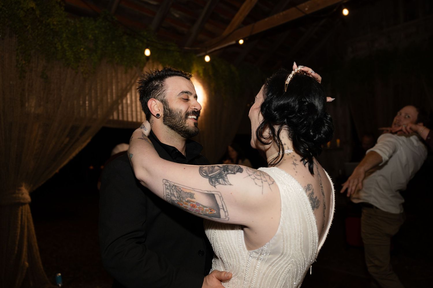 Wedding celebration in full swing with dancing couples under wooden beams and string lights.