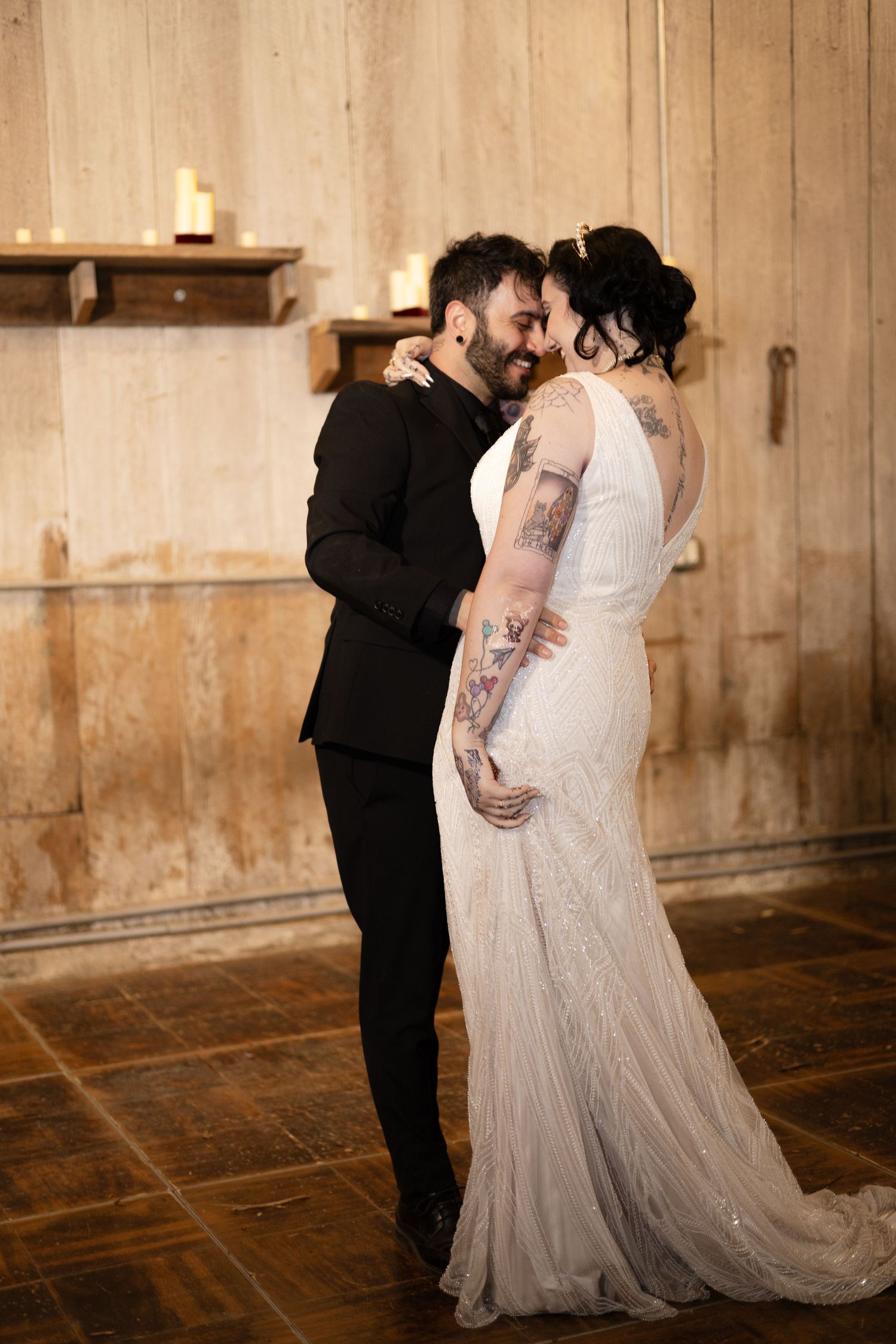 Newlyweds embrace during their first dance in a warmly lit rustic barn venue.