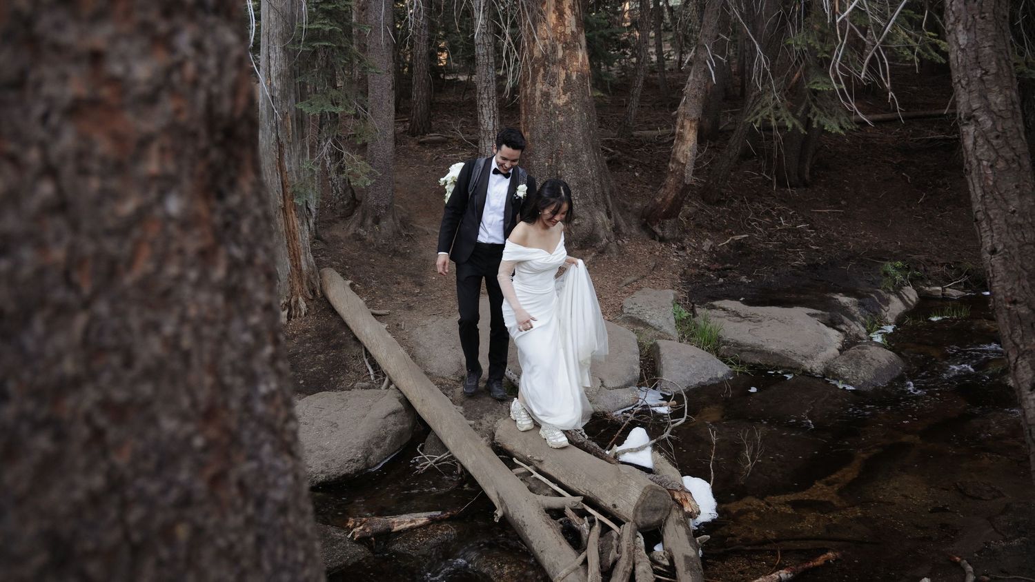 Wedding couple walking through a wooded forest path in formal attire.