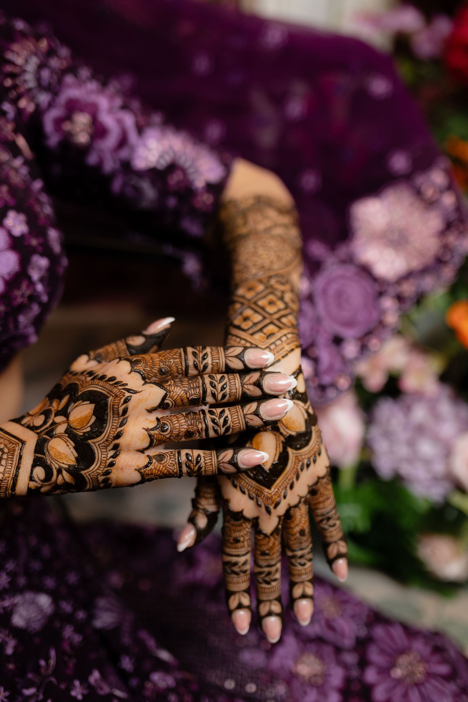 Intricate henna design on hands shown in sequence with purple flowers in the background.