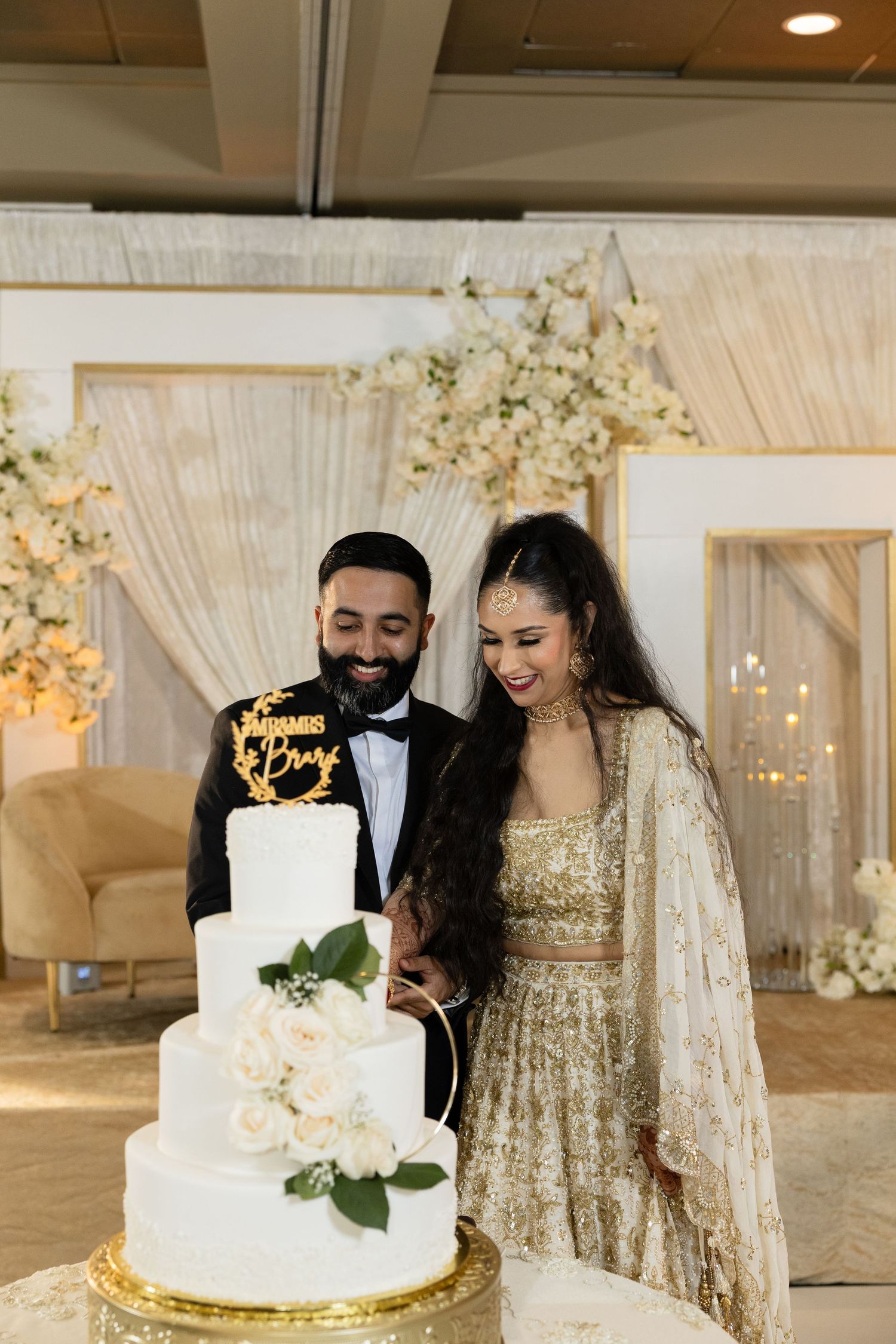 Wedding couple poses with their elegant white and gold tiered cake at reception.
