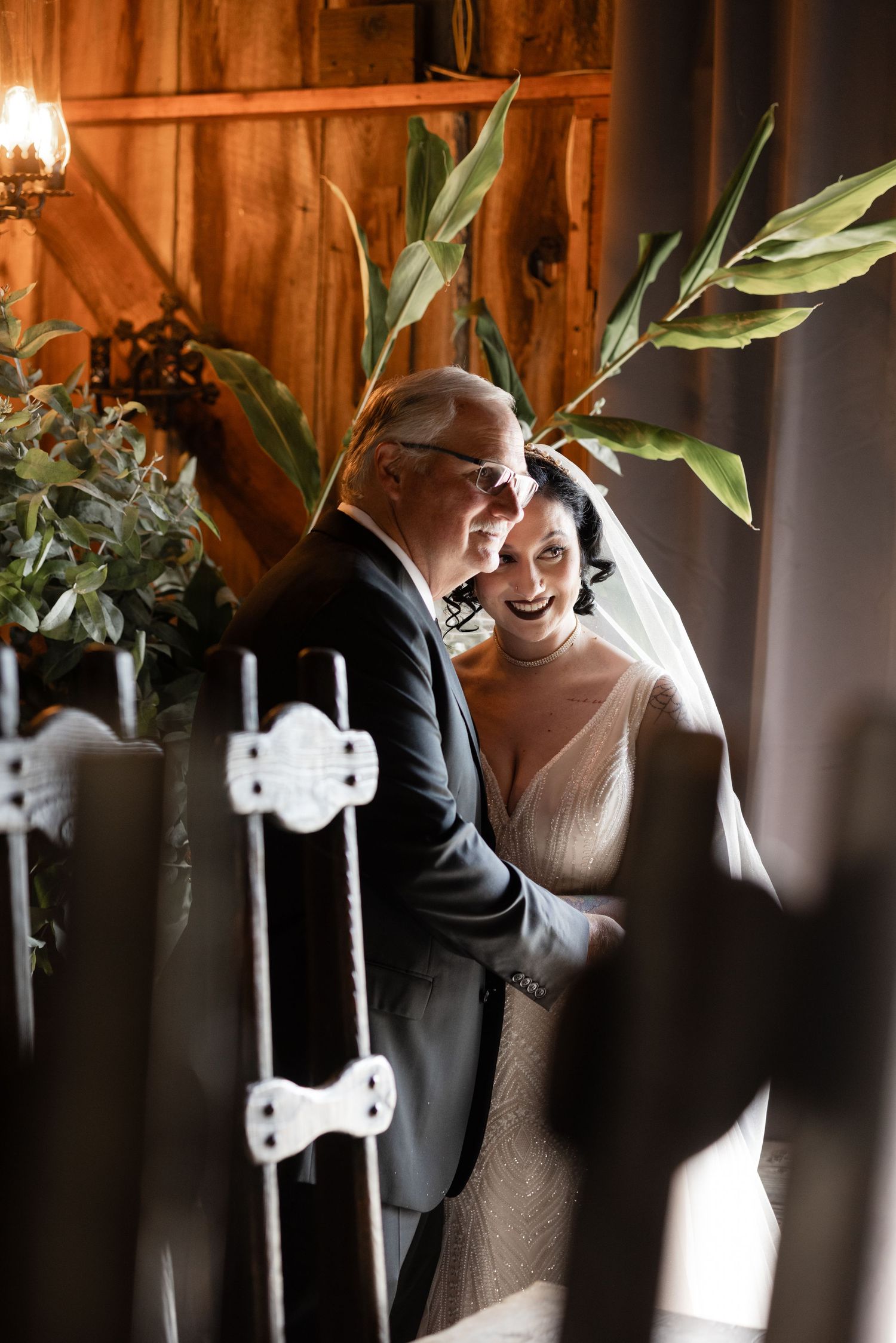 Natural light streams through a rustic barn venue with white chairs and green foliage decorations.