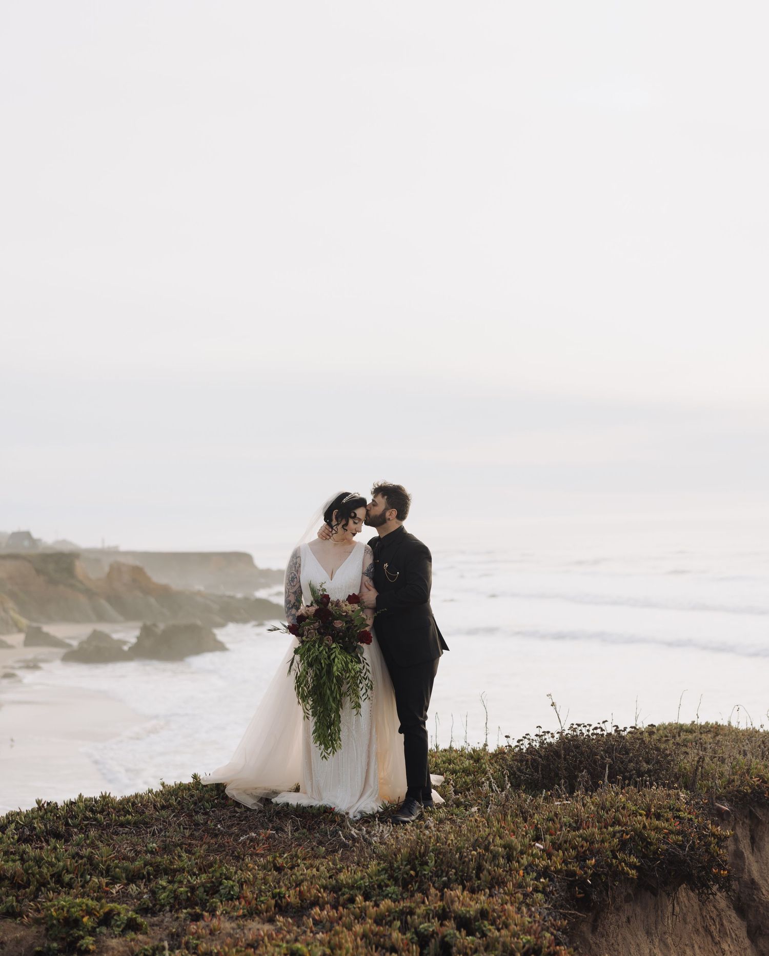 A romantic coastal wedding moment captured on rugged cliffs overlooking the Pacific Ocean.