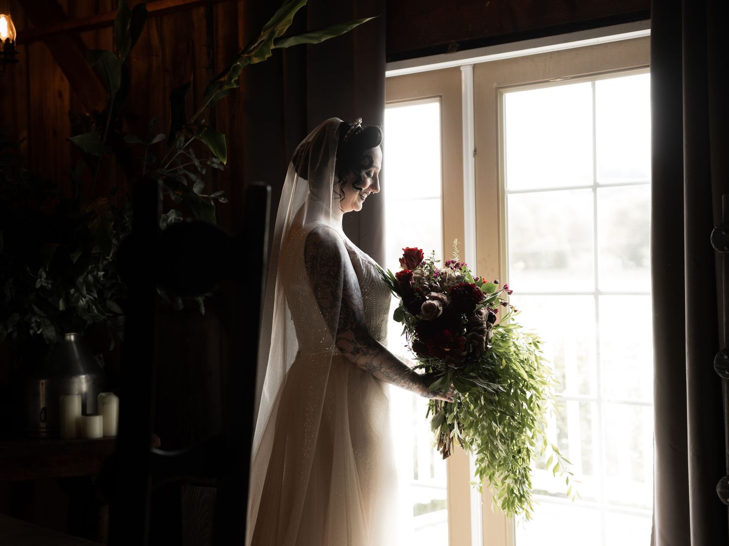 Silhouette of a bride holding a cascading bouquet while standing by a bright window.