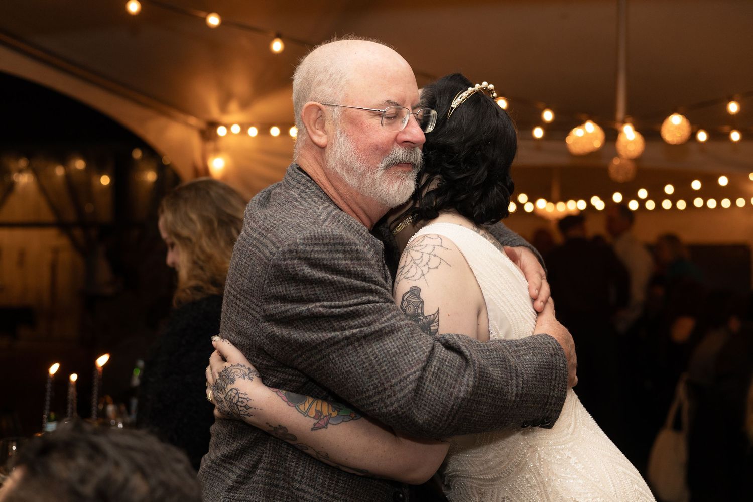 Wedding reception venue with string lights and people embracing during emotional moments.