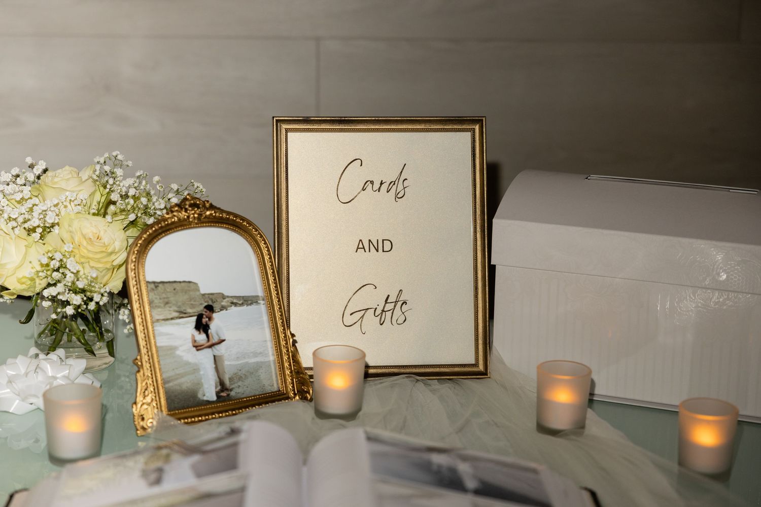 Wedding reception decor featuring gold frames and candles on white display table.
