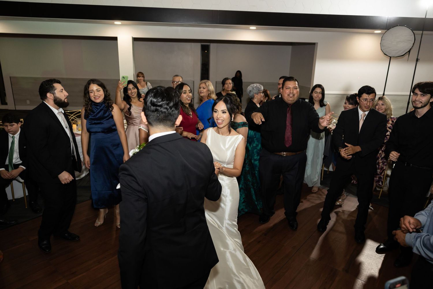 Large group of wedding guests dancing and celebrating on a dark wooden dance floor.