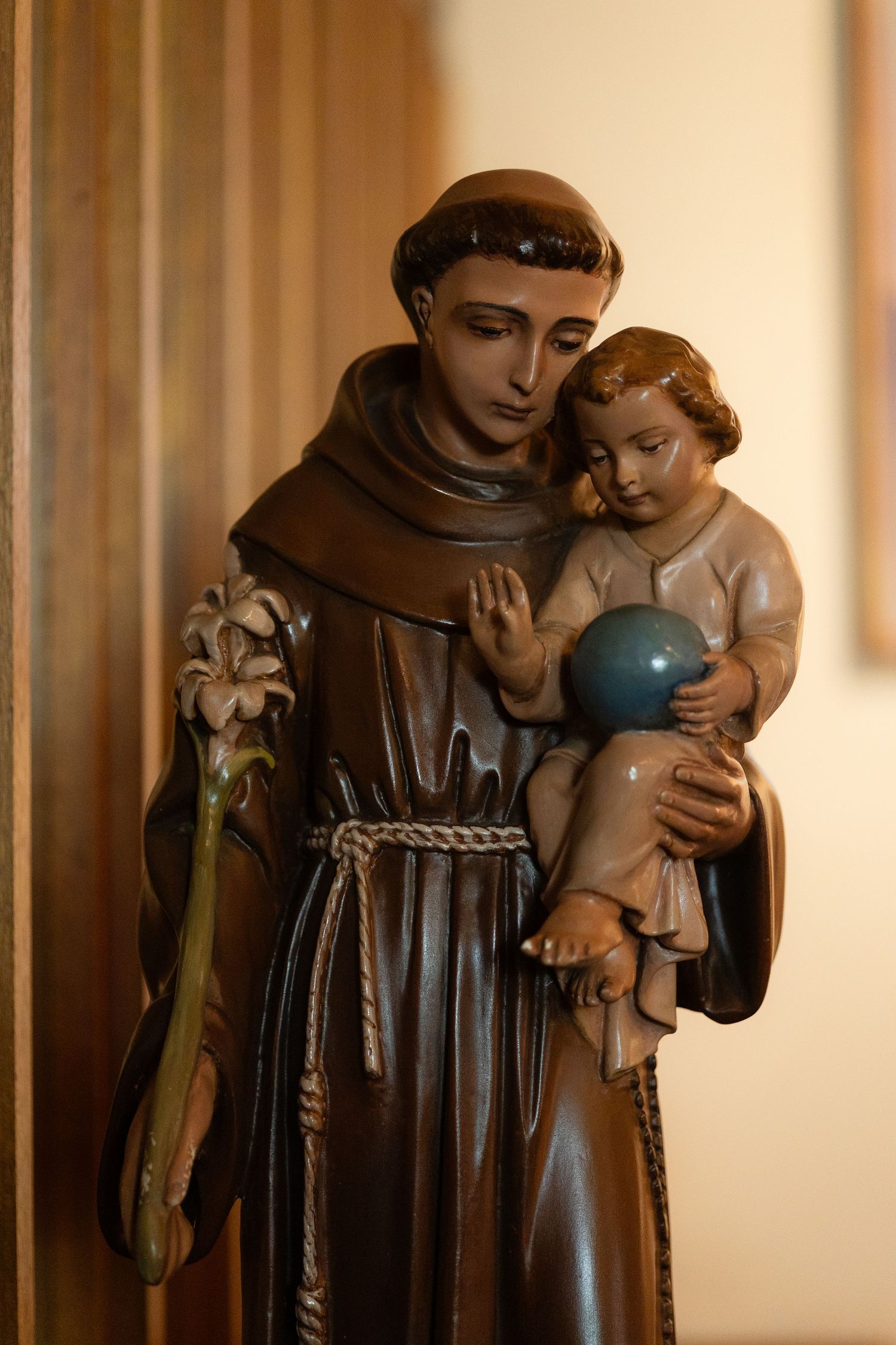 Religious statue depicting Saint Anthony holding a child in traditional brown Franciscan robes.
