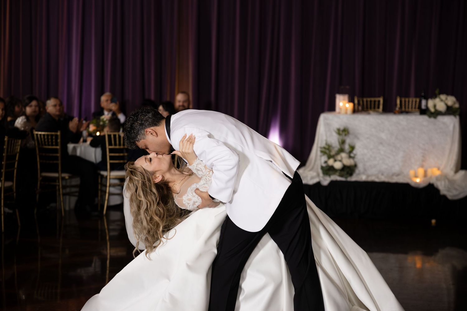 Couple shares a romantic dip and kiss during their first dance at an elegant wedding reception.