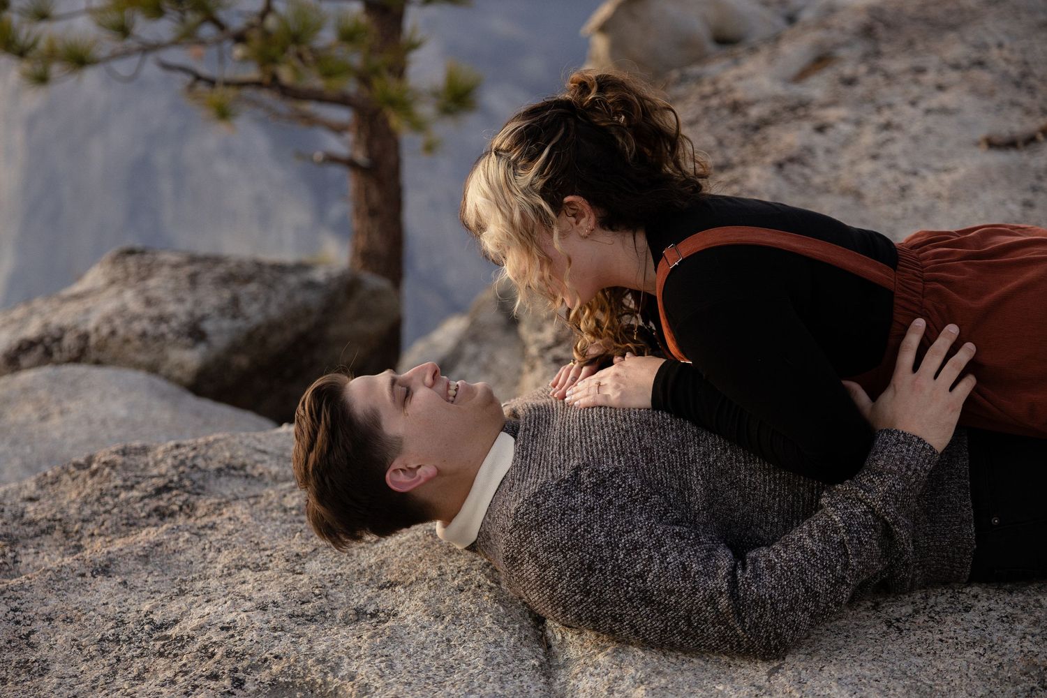 Two people lay close together on a granite rock formation with mountains in the distance.