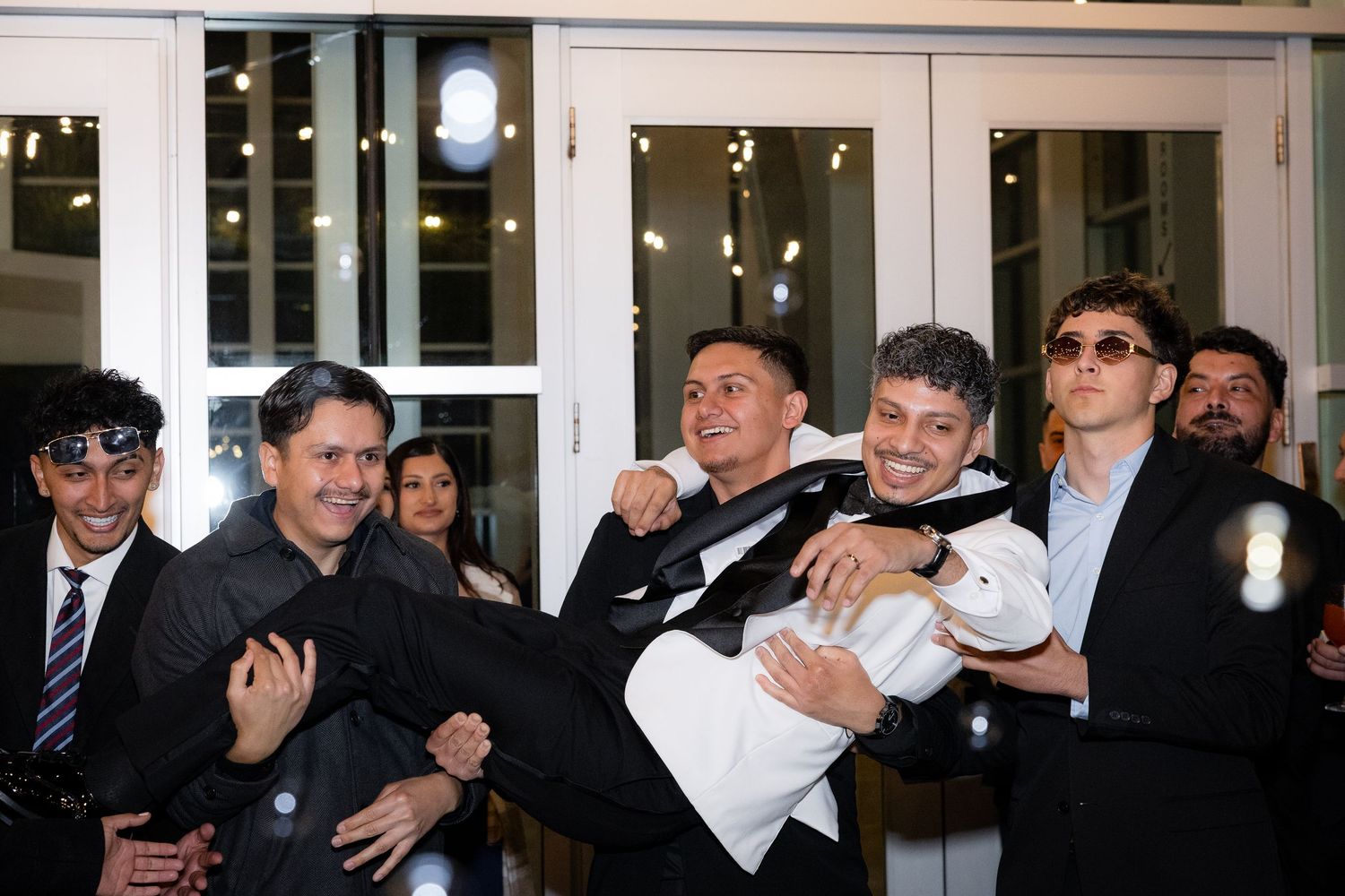 A group celebrates at a formal event in front of white French doors.