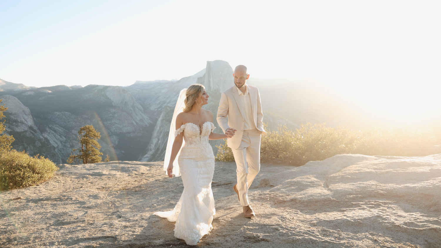 Couple walking on mountain terrain during golden hour in wedding attire.
