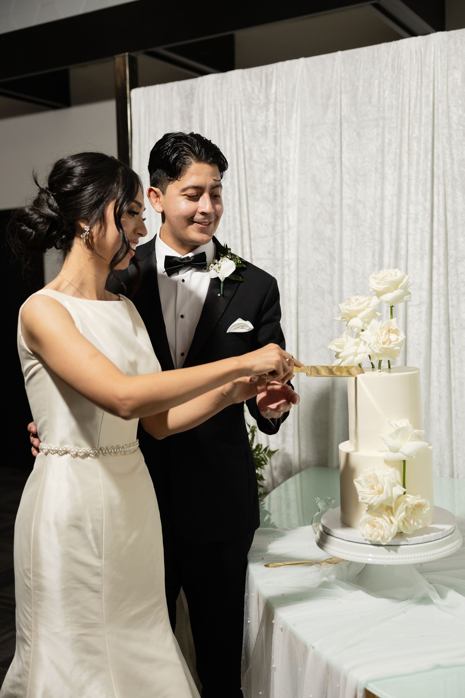 A couple cuts their elegant white wedding cake together during their reception celebration.