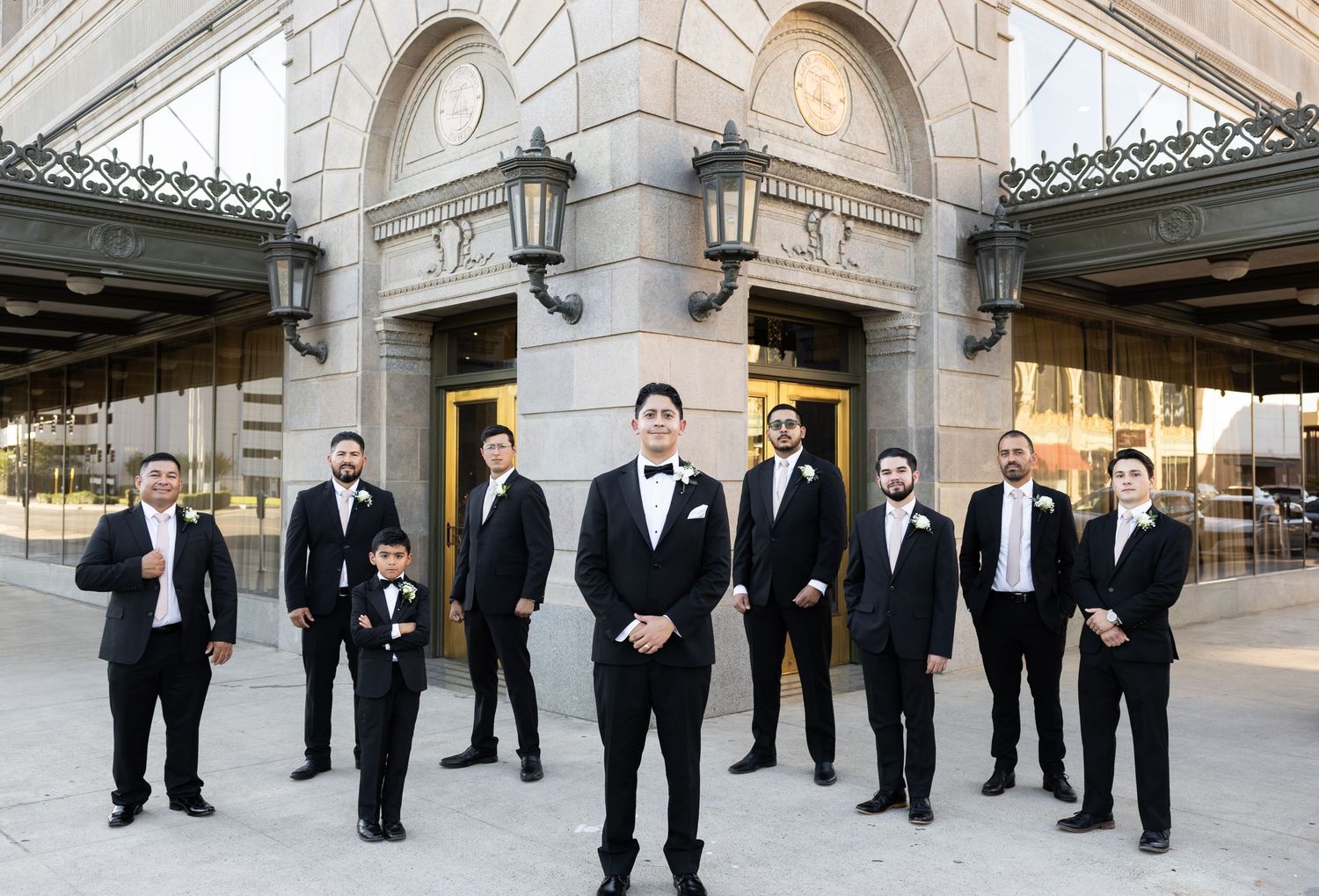 Wedding party members arranged for casual group photos outside stone building.
