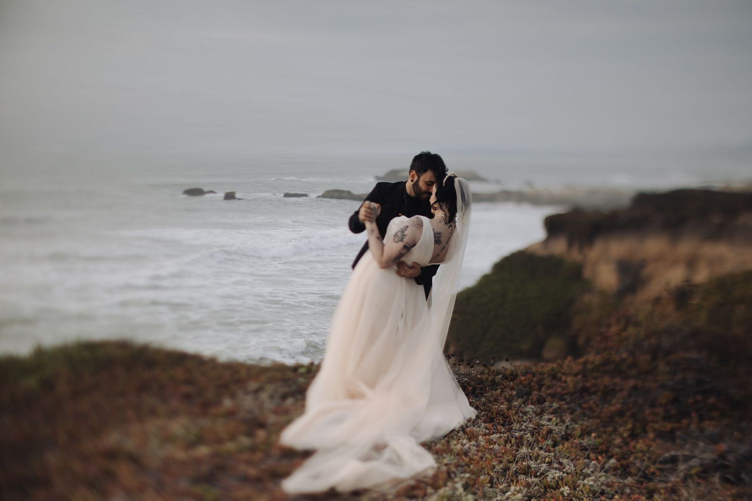 Couple walking along a dramatic coastal cliff at sunset with flowing dress.
