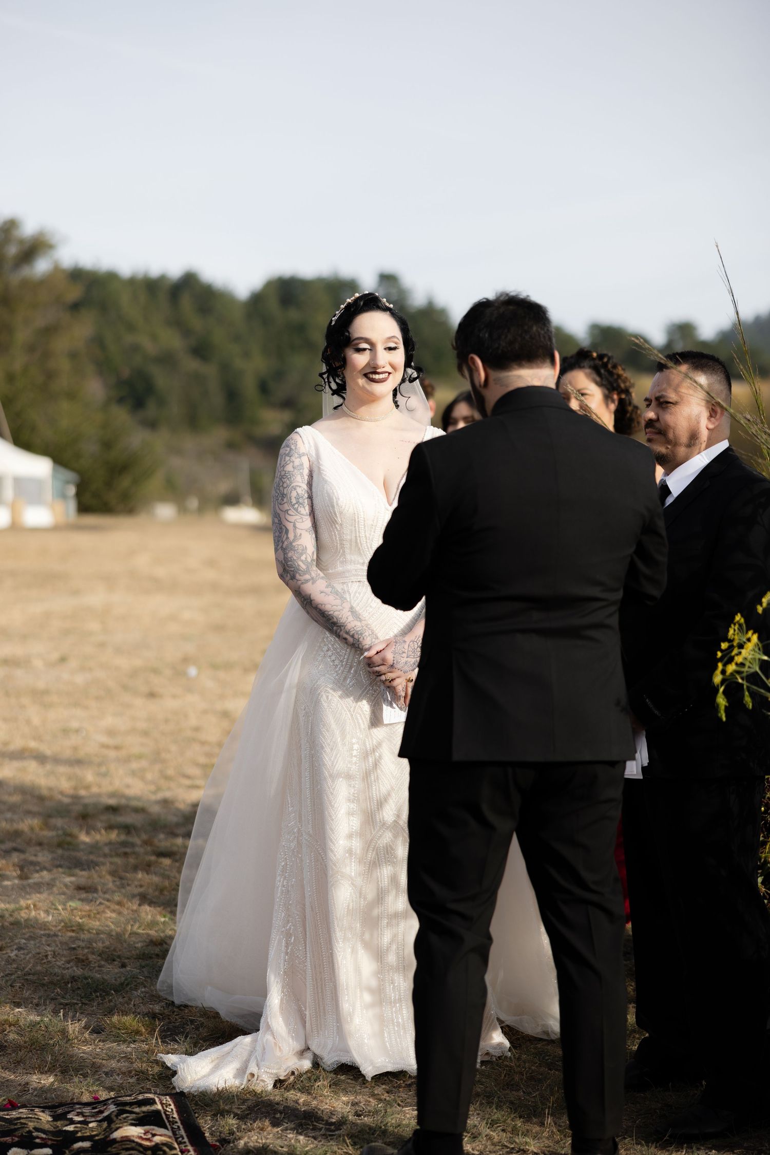 Intimate moment during outdoor wedding ceremony with wooden arch and natural backdrop.