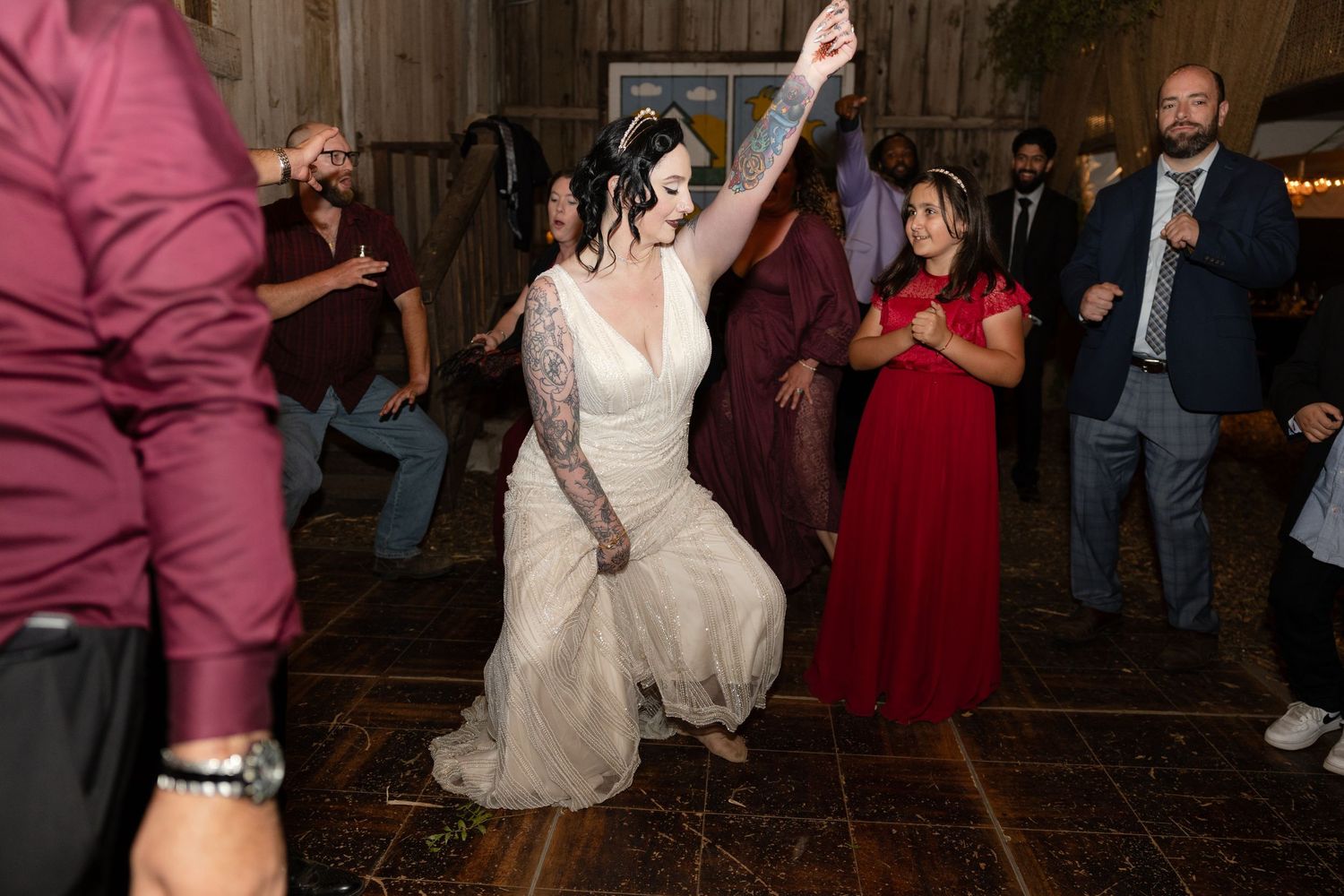 Wedding guests dance energetically on a rustic wooden dance floor during a reception celebration.