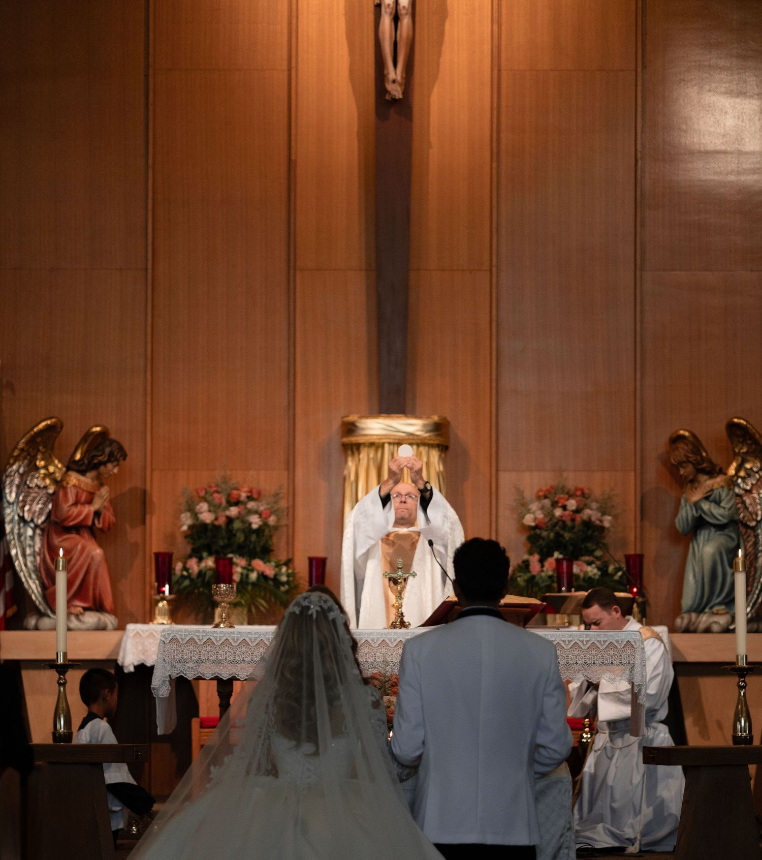 A traditional Catholic wedding ceremony taking place at an altar with angel statues and floral arrangements.