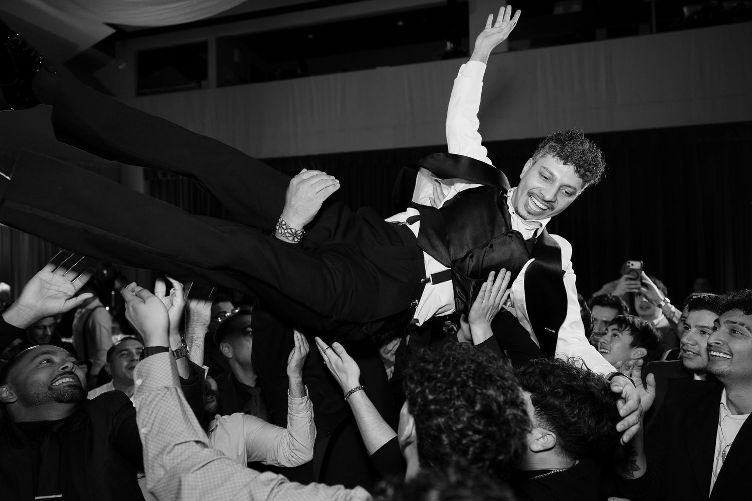 Black and white photo captures crowd surfing moment during wedding celebration.