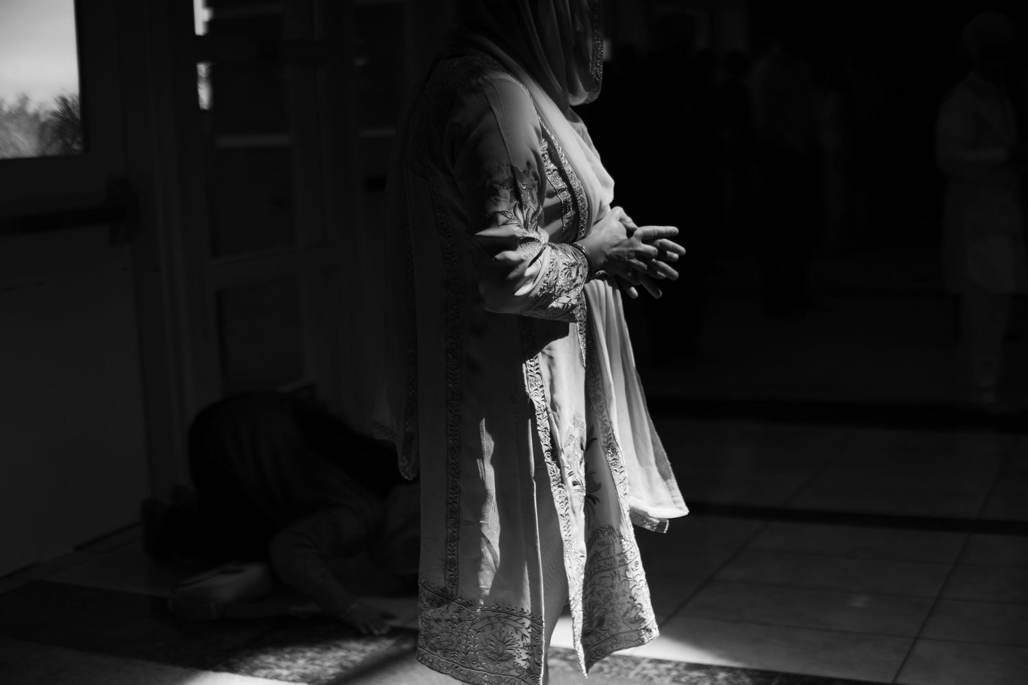 A black and white photograph shows a figure in flowing clothing standing in a dark, atmospheric interior space.