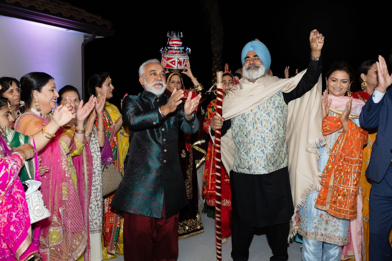 A group of people in traditional Indian attire celebrate joyfully at a festive gathering.