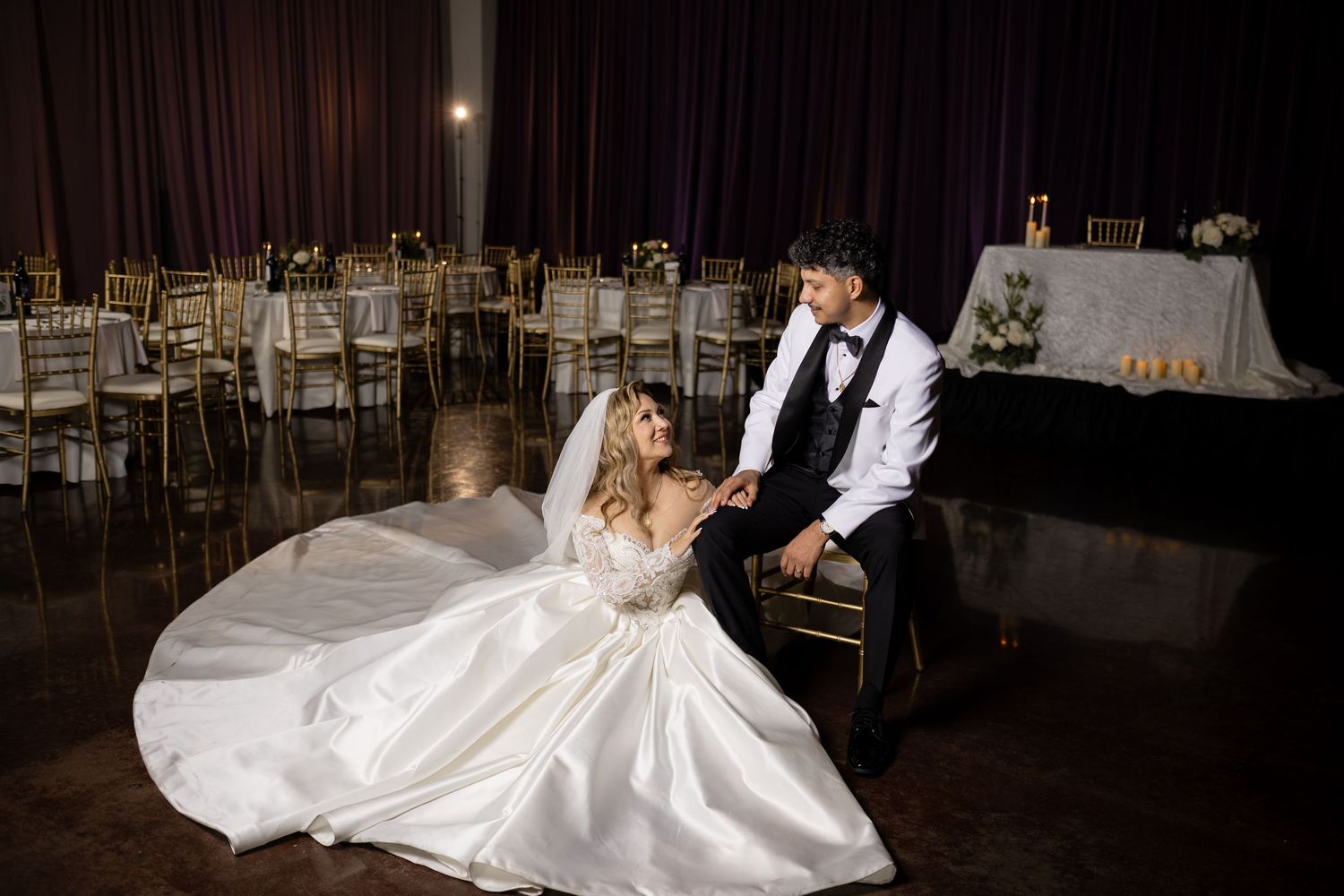 A stunning bridal gown with long train creates artistic shapes on a dark ballroom floor.