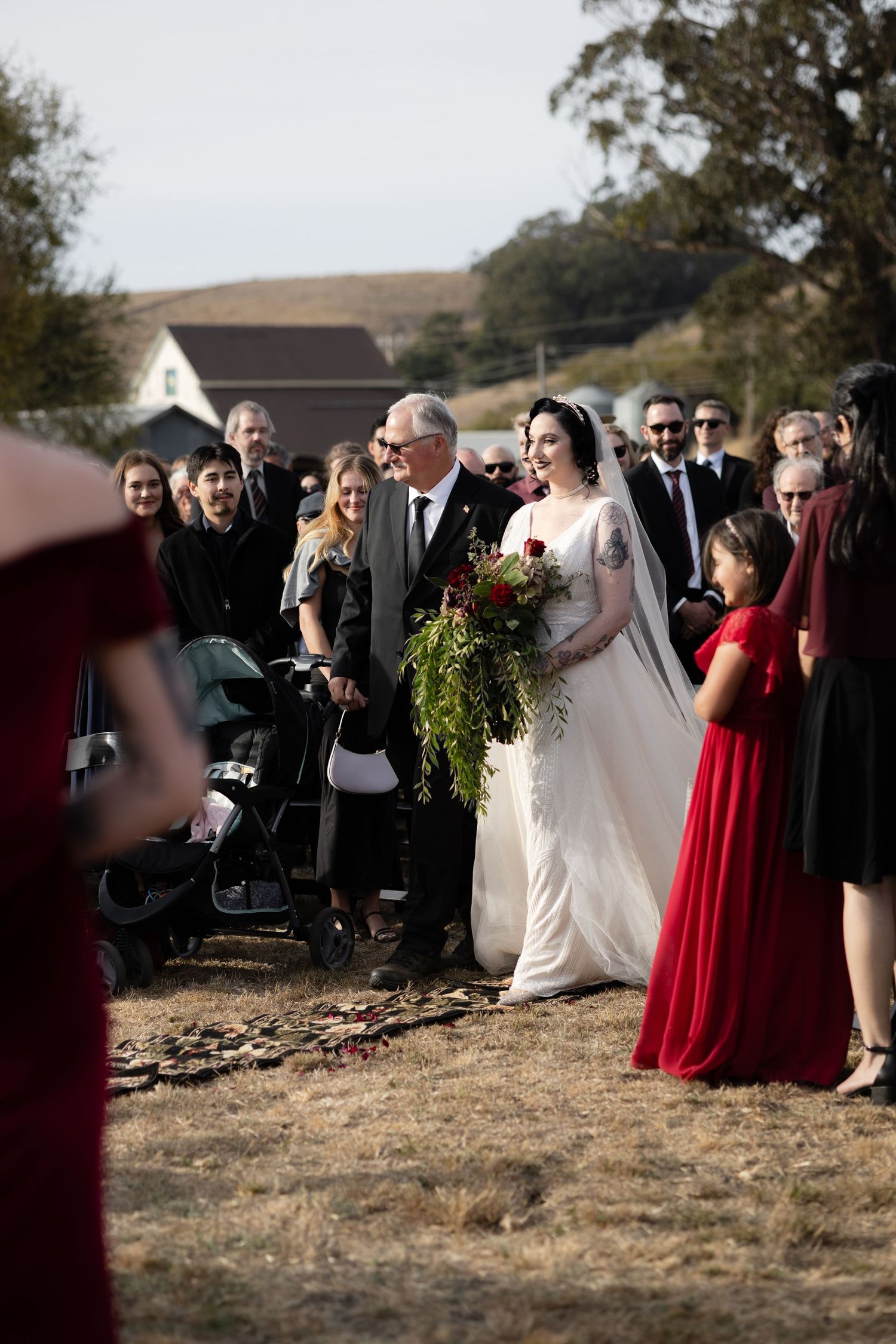 Outdoor wedding ceremony with attendees in formal attire gathered on a hillside.