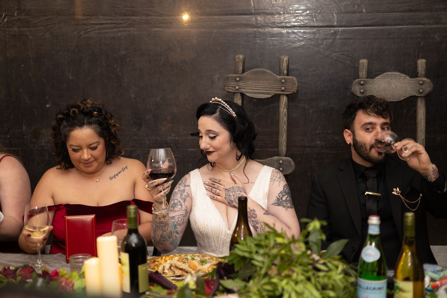 Wedding reception dinner table with candles and greenery decorations against dark walls.