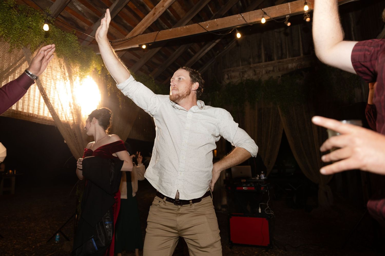 Wedding reception dance floor filled with energy as guests celebrate under rustic wooden rafters.