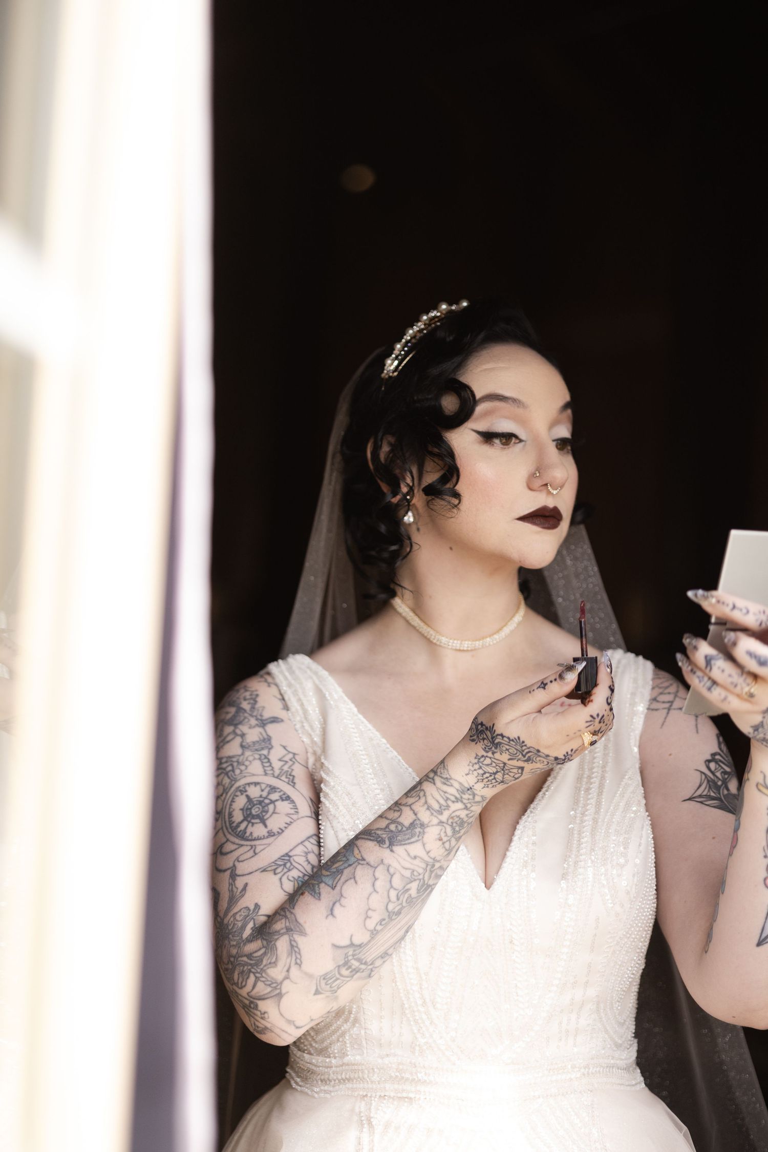 Side profile of bride in white v-neck dress with dramatic makeup and visible tattoos.