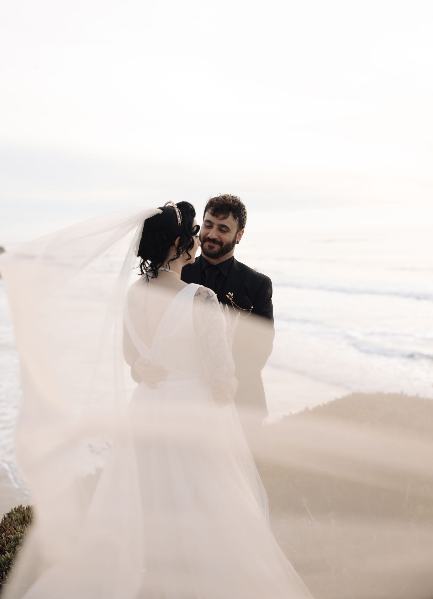 Ethereal wedding photography with flowing white dress against coastal backdrop.
