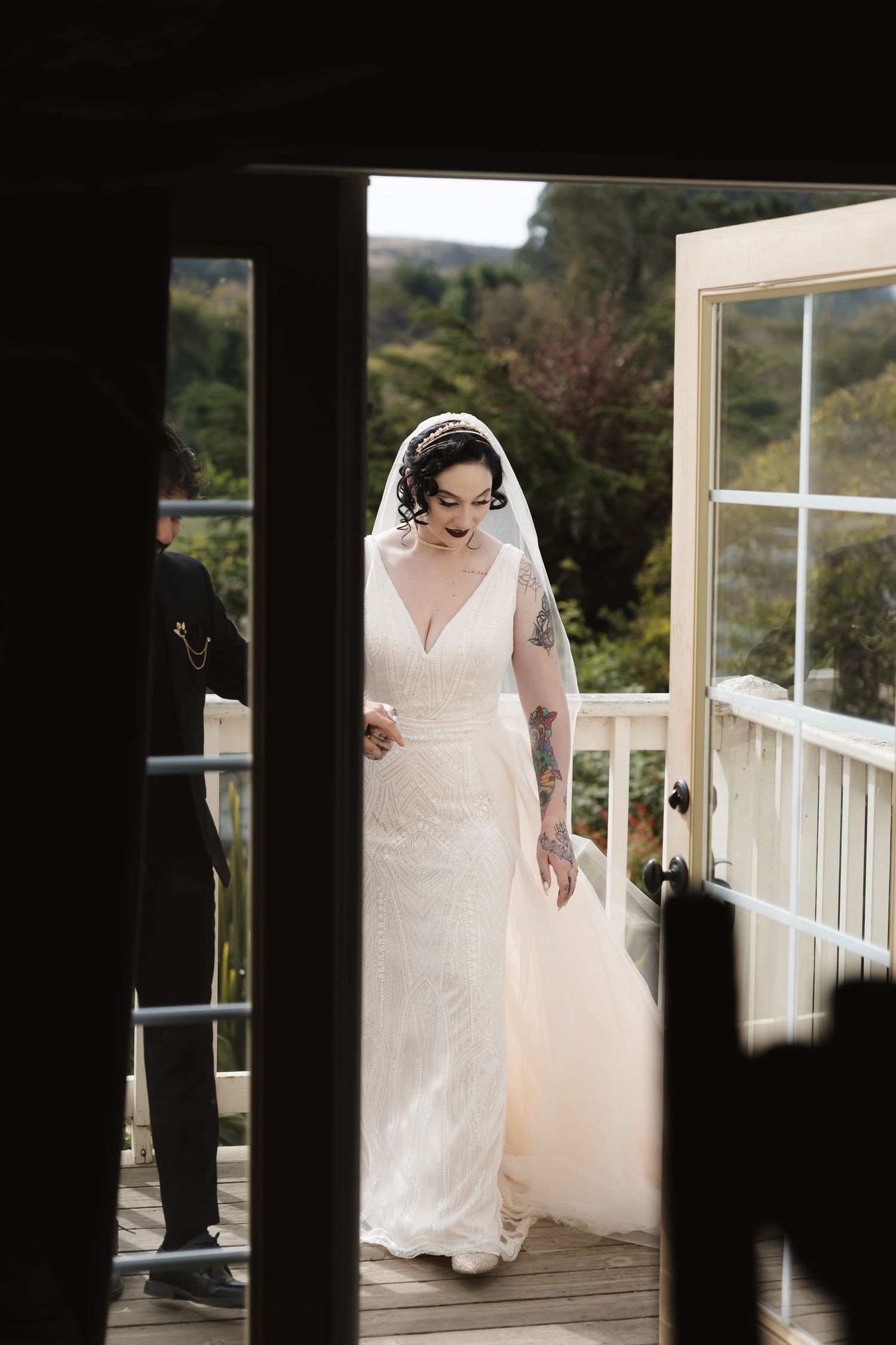 Elegant bride in fitted white dress and veil standing on outdoor deck.