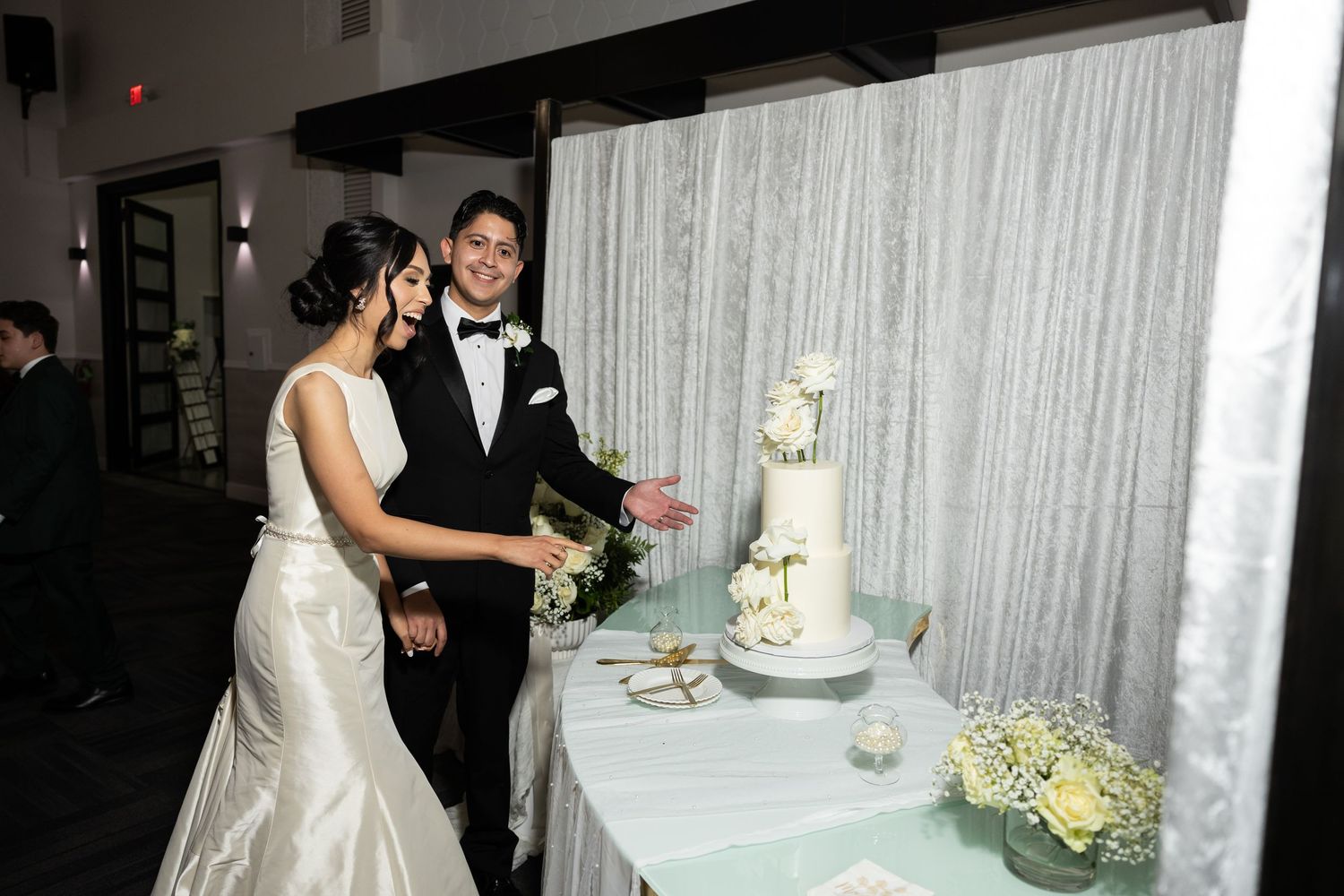 Wedding reception scene with couple cutting their elegant white tiered cake.