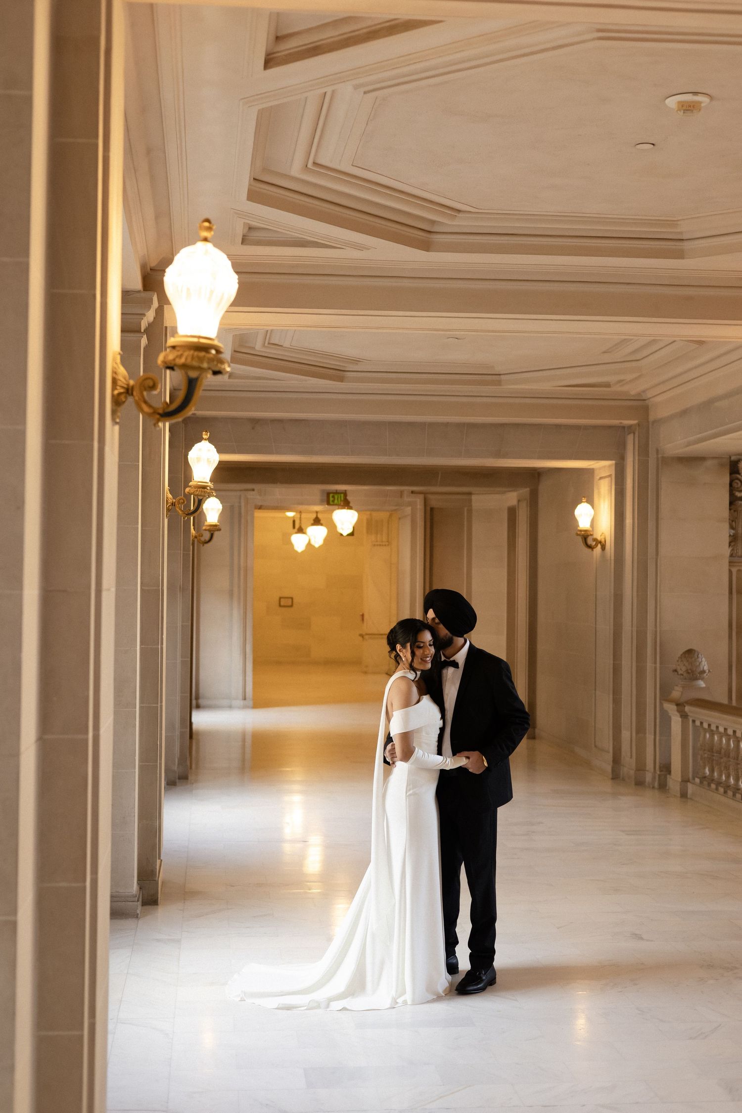 An elegant marble hallway with chandeliers serves as backdrop for wedding photography.
