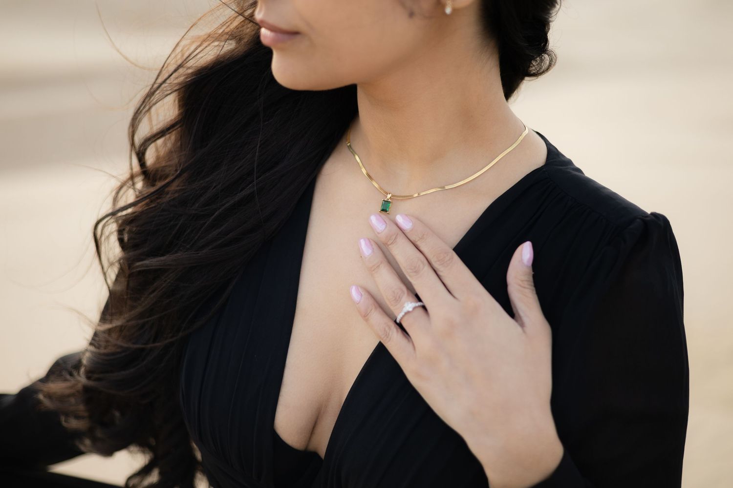 Woman in black blazer wearing delicate necklace with hand placed on chest.