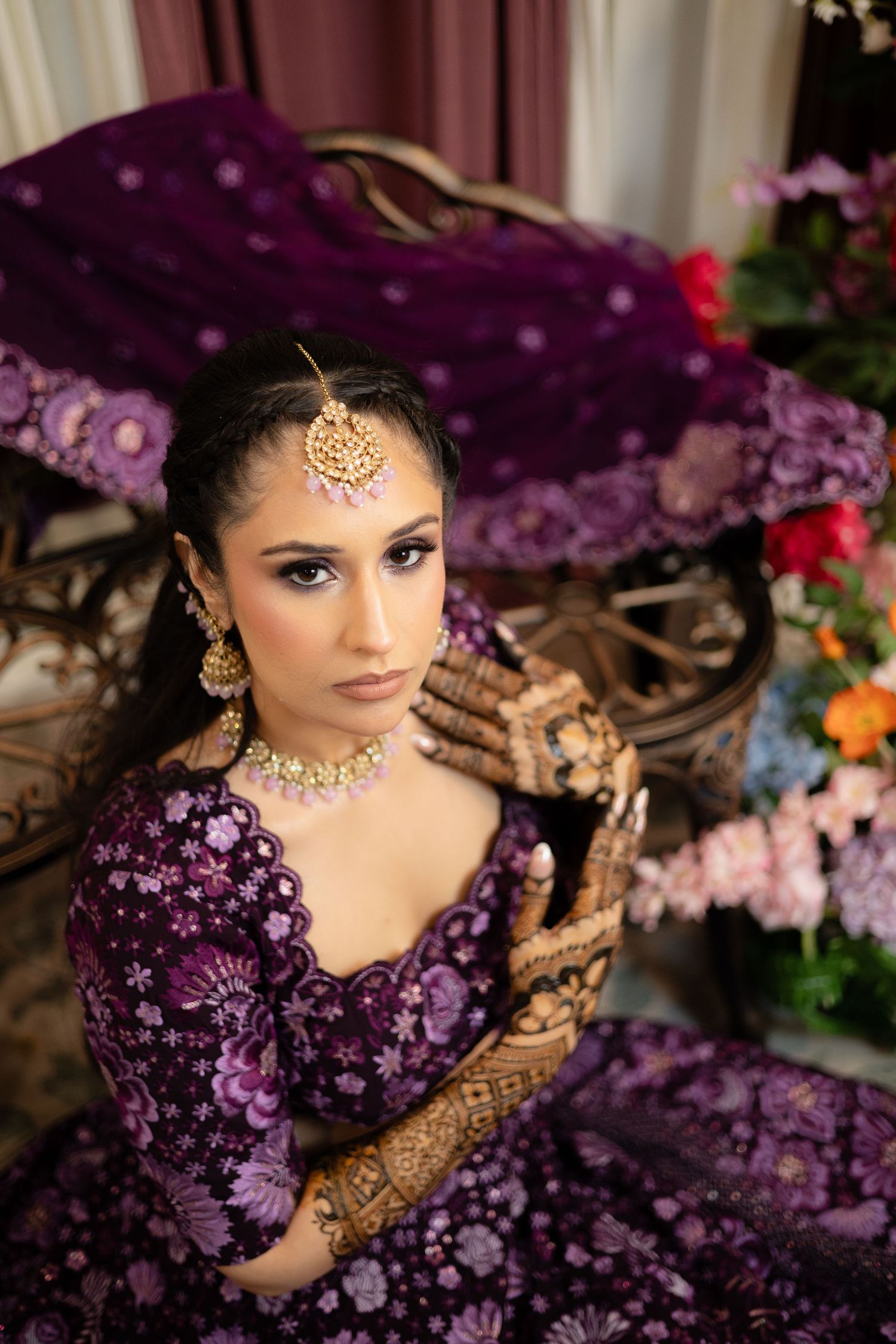 Traditional bridal jewelry and purple attire photographed with dramatic lighting and floral decorations.