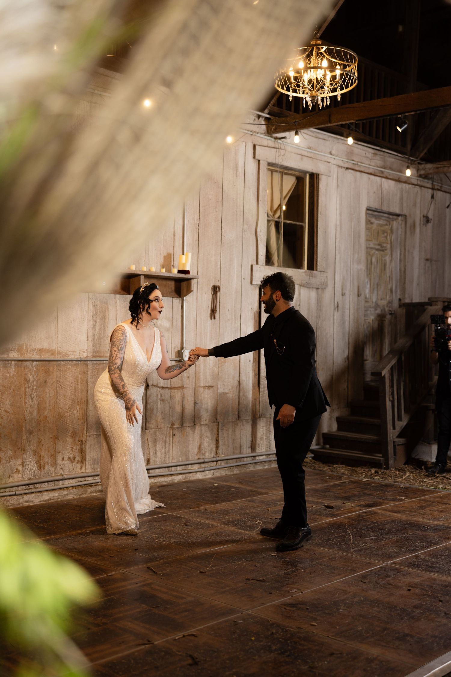 Couple dancing in a rustic barn venue with string lights overhead and wooden walls.