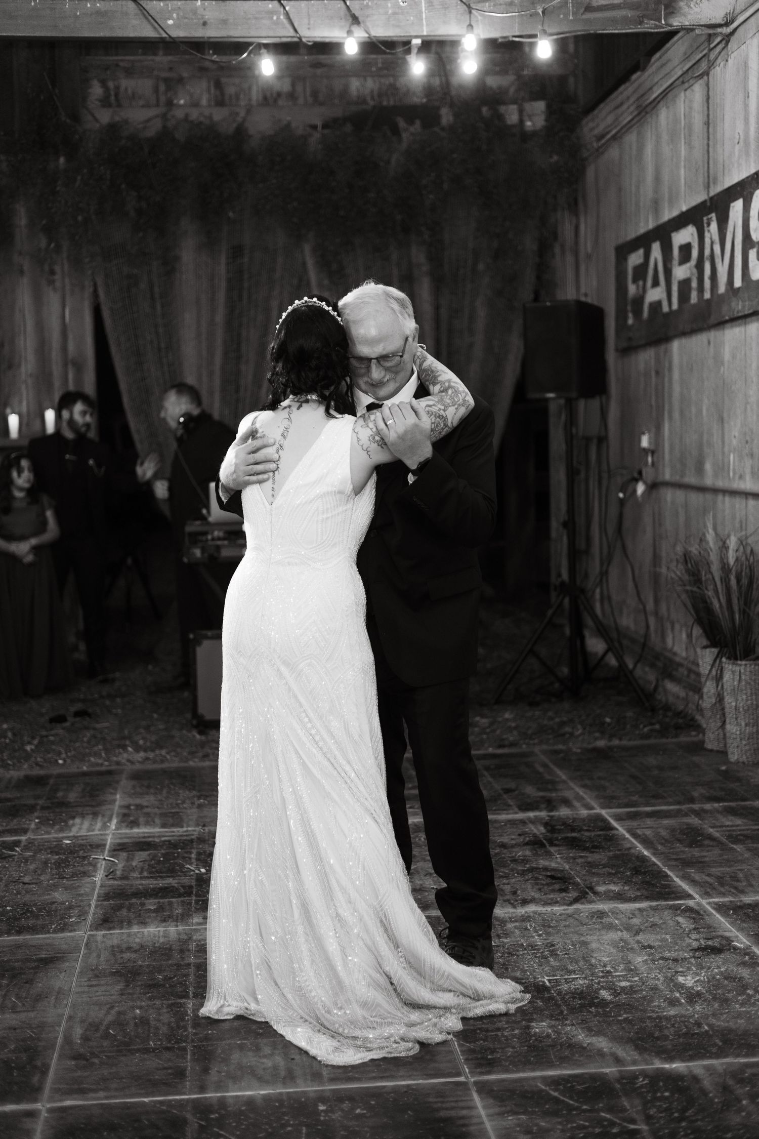 Black and white photo of a wedding dance in a rustic barn setting with ambient lighting.