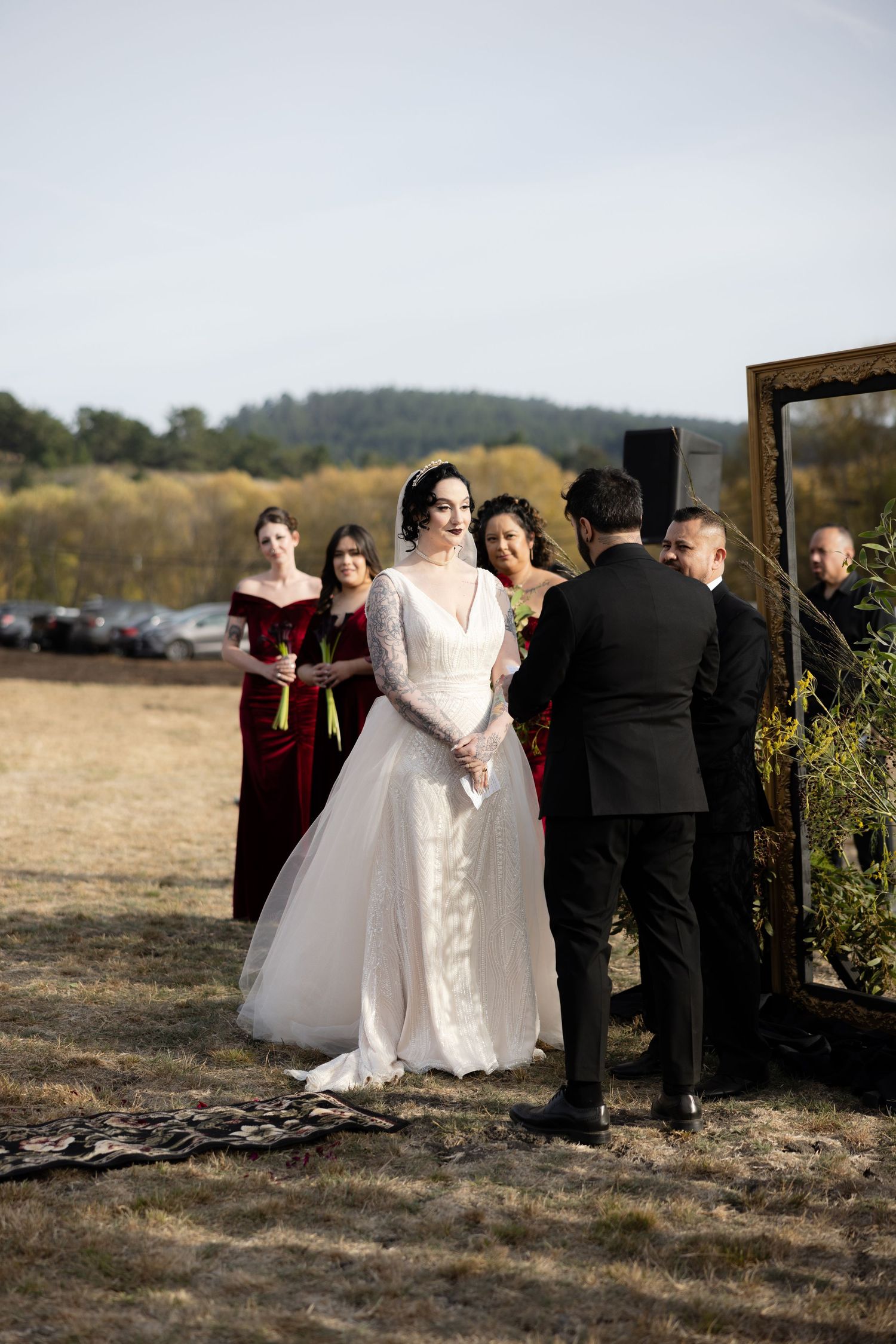 Wedding party arranges around rustic wooden arch for ceremony in autumn field.
