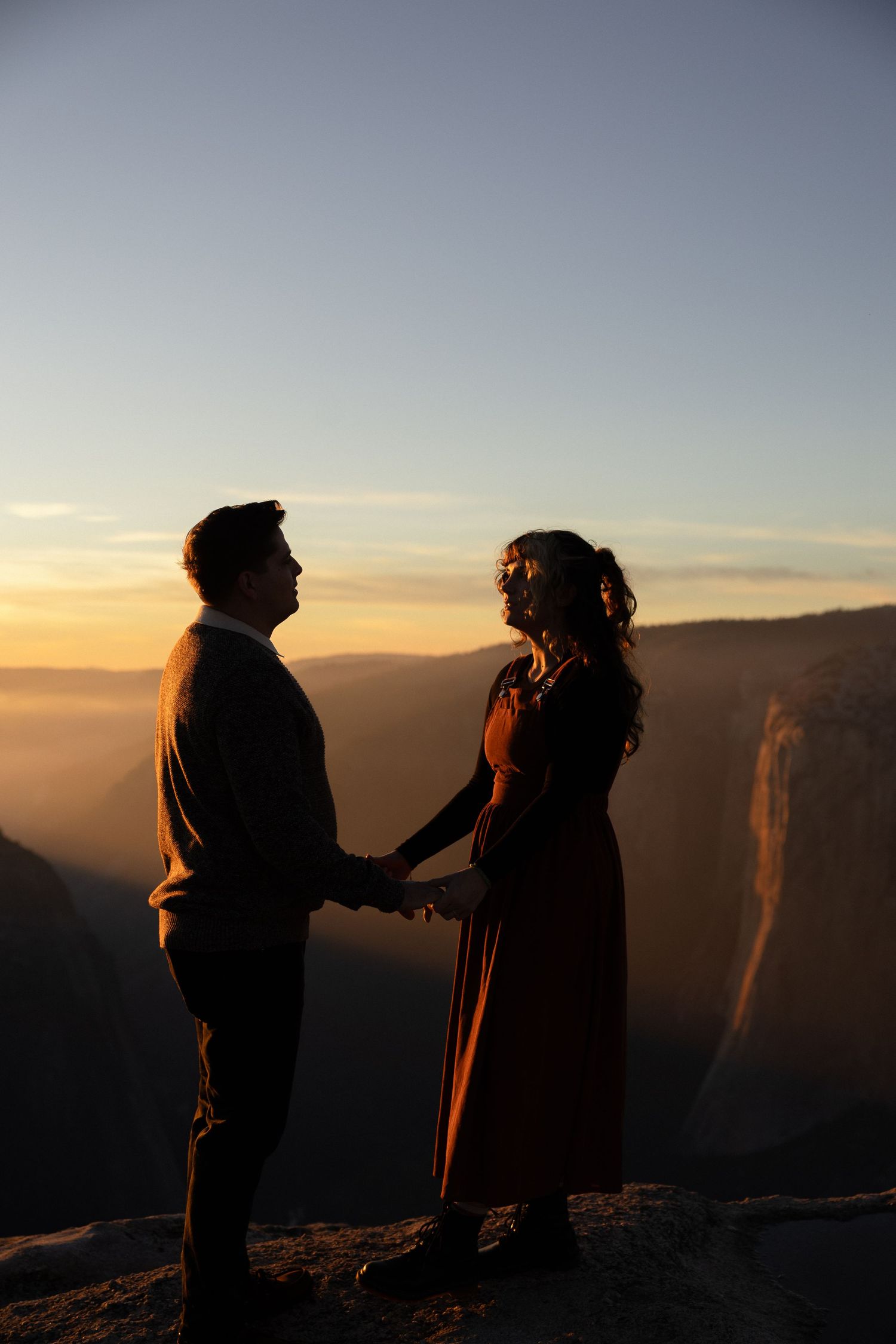 A silhouetted couple stands together on a cliff edge during a golden sunset.