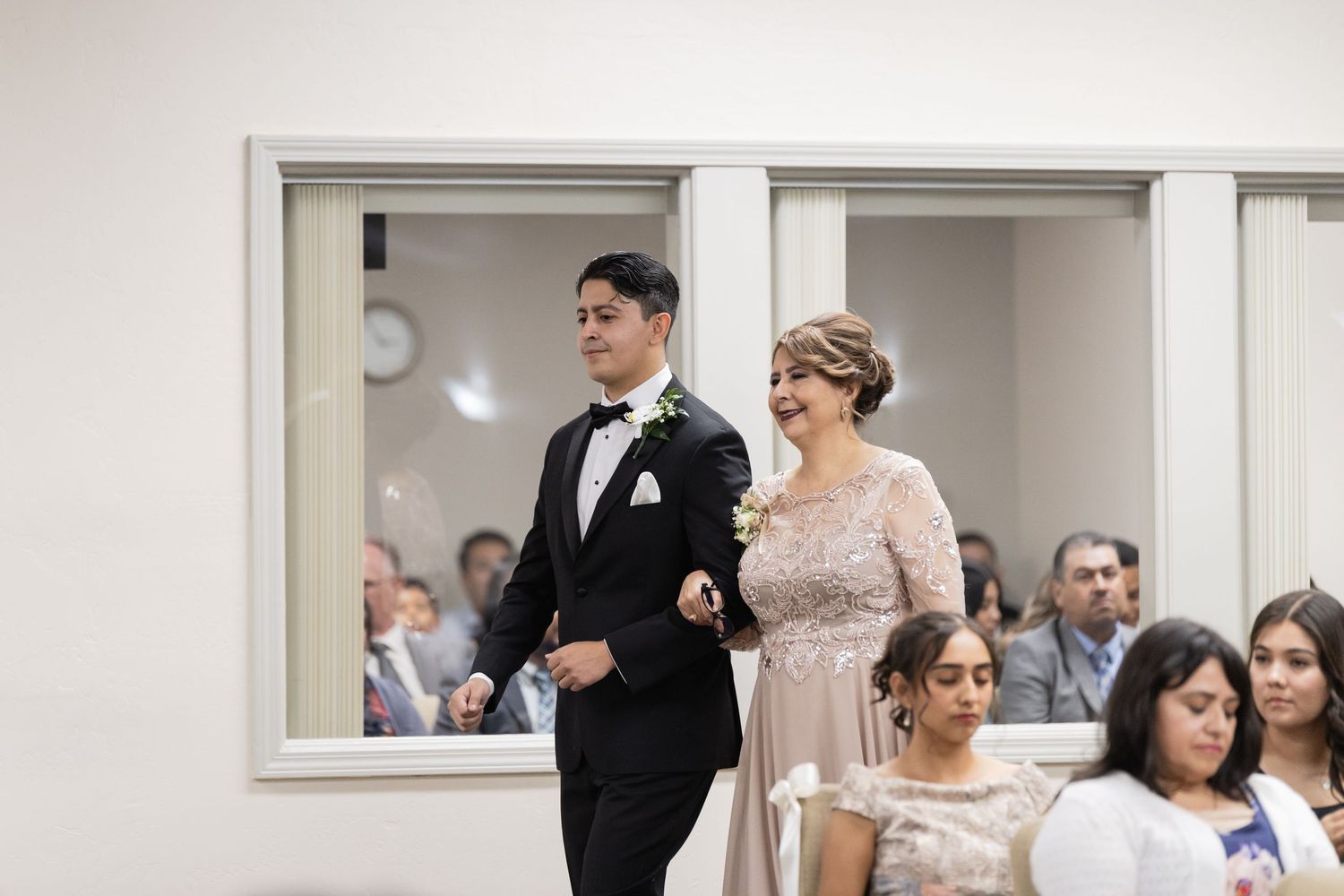 A couple in formal attire walking arm in arm through a hallway at an event.