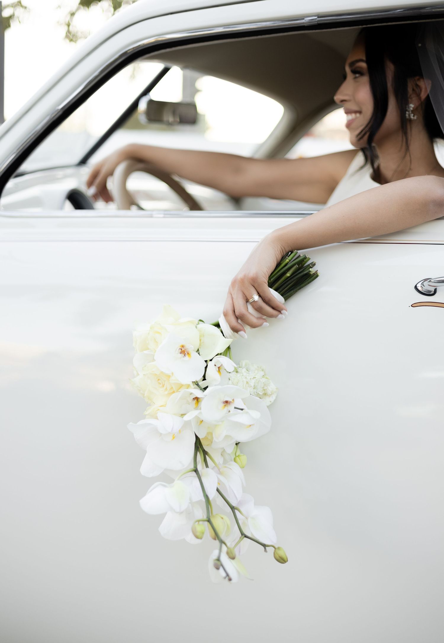 White orchid bouquet held through car window against light gray vehicle exterior.