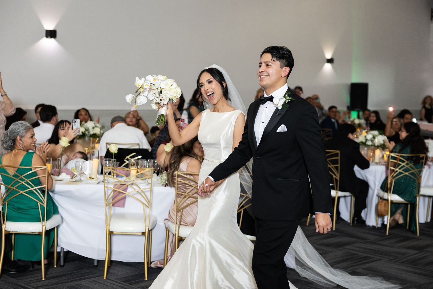 Wedding reception celebration with guests and decorated tables in bright indoor venue.