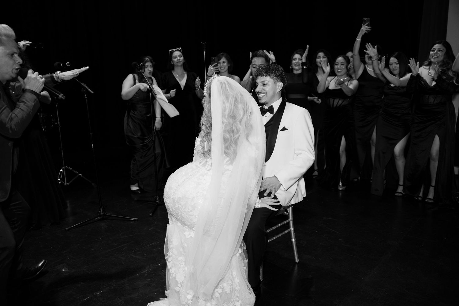 A black and white photo captures an intimate wedding dance moment surrounded by celebrating guests.