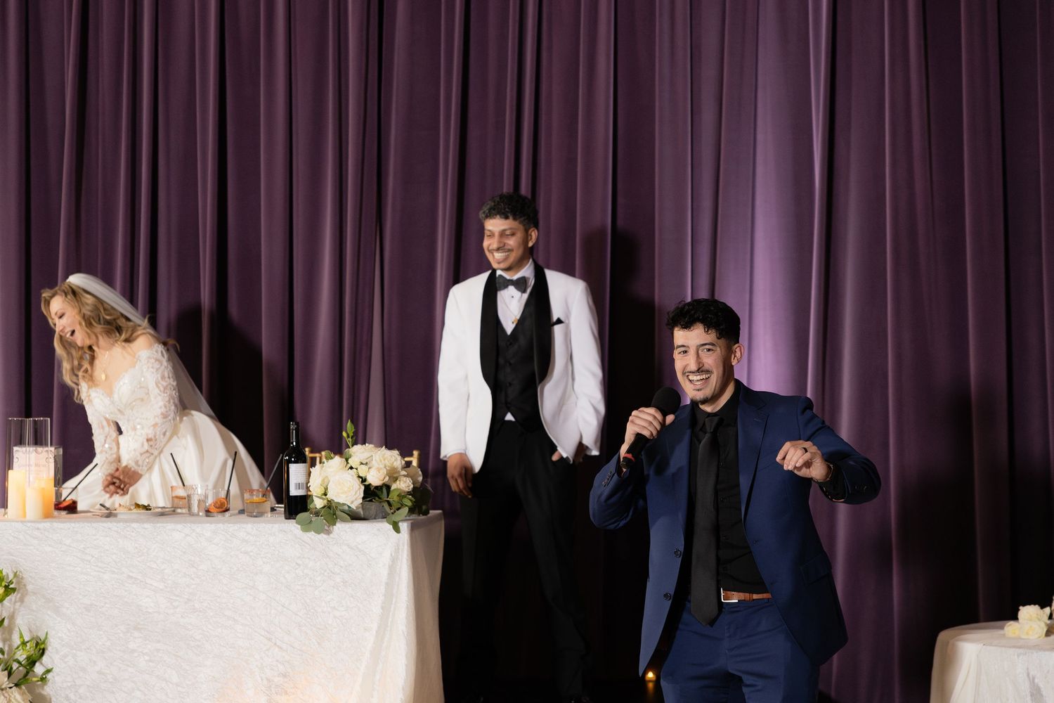 Wedding reception scene at head table with festive moments and purple backdrop.