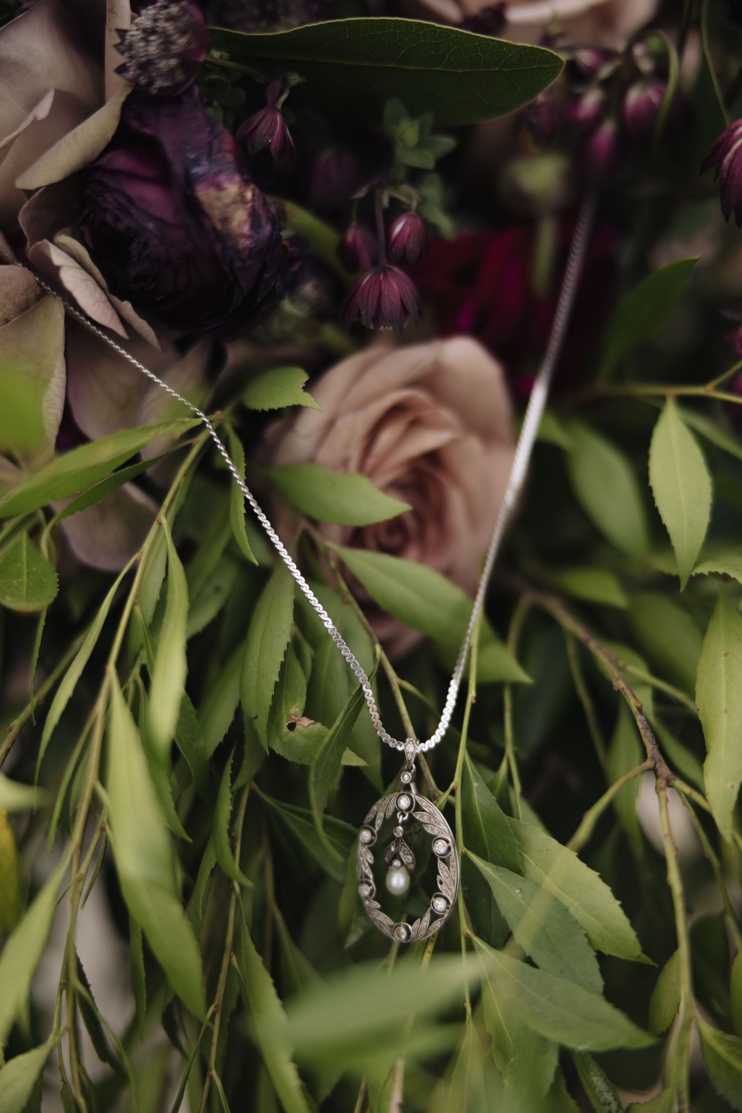 Pearl necklace draped elegantly among dark purple flowers and green foliage.